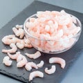 Frozen raw peeled shrimps in a glass bowl on a dark background, square