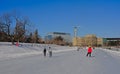 Frozen rideau canal with skaters, highrise office buildings and trees on the embankment