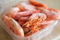 Frozen shrimps in plastic container box on kitchen table for cooking.Delicious prawns in ice ready for meal preparation.Enjoy