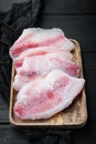 Frozen tilapia fish meat, on black wooden table