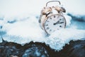 Frozen time. A clock on an ice next to the water. Extreme weather situation. Snow falling on a clock in a nature.