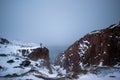 Frozen waterfall on the background of hills on the Kola Peninsula and a man standing on the edge of the cliff and looking into the