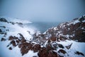 Frozen waterfall on the background of hills on the Kola Peninsula and a man standing on the edge of the cliff and looking into the