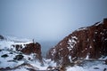 Frozen waterfall on the background of hills on the Kola Peninsula and a man standing on the edge of the cliff and looking into the