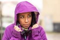 A frozen young woman in a rain jacket has a hood on and protects her head from the rain and wind during late autumn Royalty Free Stock Photo