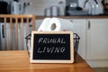 Frugal living, save money, live cheap concept with toilet paper basket and Frugal living text in frame on kitchen table