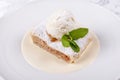 Fruit apple strudel cake served with ice cream, mint leaf and vanilla sauce. Classical austrian dessert on white plate