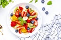 Fruit and berry salad with fresh strawberries, blueberries, banana, kiwi, orange and mint leaves, white table background, top view Royalty Free Stock Photo