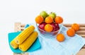 The fruit bowl with red apple,green apple and orange put beside dish of yellow corn,three oranges put beside glass bow