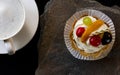 Fruit cake with cherries, grapes and plum stands on a wild stone next to a white cup of coffee with a foam Royalty Free Stock Photo