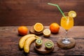 Fruit cocktail with a straw garnished with a slice of lemon in a large glass on a wooden table next to oranges bananas Royalty Free Stock Photo