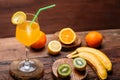 Fruit cocktail with a straw garnished with a slice of lemon in a large glass on a wooden table next to oranges bananas Royalty Free Stock Photo