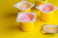 Fruit flavoured yogurt in yellow plastic cups on bright yellow background with silver foil lid in foreground