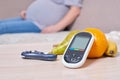 Fruit and glucose meter on table, pregnant woman on sofa, blood sugar control concept Royalty Free Stock Photo