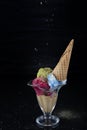 Fruit ice cream scoops overhead on a cornet, served with several colorful spoons isolated on black background