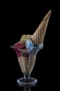 Fruit ice cream scoops overhead on a cornet, served with several colorful spoons isolated on black background