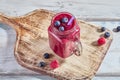 Fruit pink smoothie with berries in a glass jar on a wooden white table. Copy space