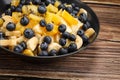 Fruit salad with blueberries, banana, orange, apple and kiwi on a black plate and wooden table. Vitamin cocktail. Royalty Free Stock Photo