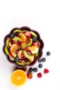 Fruit Salad in purple Bowl on white Table, fruit and berries scattered on table