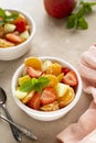 Fruit salad in white bowl with mint and fresh apple, strawberry, tangerines, pineapple and honey Royalty Free Stock Photo