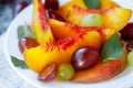 Fruit salad in white plate. Snack of fresh peaches, grapes, dogwood, plums, and mint leaves. Healthy Breakfast Royalty Free Stock Photo