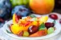 Fruit salad in white plate. Snack of fresh peaches, grapes, dogwood, plums, and mint leaves. Healthy Breakfast Royalty Free Stock Photo