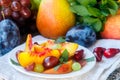 Fruit salad in white plate. Snack of fresh peaches, grapes, dogwood, plums, and mint leaves. Healthy Breakfast Royalty Free Stock Photo