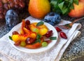 Fruit salad in white plate. Snack of fresh peaches, grapes, dogwood, plums, and mint leaves. Healthy Breakfast Royalty Free Stock Photo