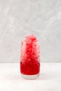 Fruit shaved ice in tall glass. Slushie - drink on grey background. Refreshing summer drink. Selective focus, copy space