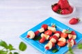 Fruit skewers with strawberry and banana on a blue square plate on a light wooden background. Dishes party, children, holiday Royalty Free Stock Photo