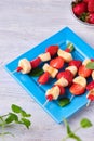 Fruit skewers with strawberry and banana on a blue square plate on a light wooden background. Dishes party, children, holiday Royalty Free Stock Photo