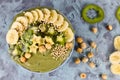Fruit smoothie bowl dyed green with barley powder, topped with star shaped banana, kiwi, hazelnut and puffed quinoa grain on gray