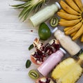 Fruit smoothies or milkshakes of various colors in glass bottles with tropical fruits on white wooden surface, overhead view. From Royalty Free Stock Photo