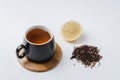 Fruit tea in a black mug on a bamboo support, lemon segment and dried tea isolated on white background