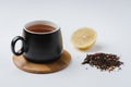 Fruit tea in a black mug on a bamboo support, lemon segment and dried tea isolated on white background