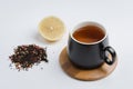 Fruit tea in a black mug on a bamboo support, lemon segment and dried tea isolated on white background