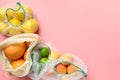 Fruits and citrics in reusable eco-friendly mesh bags on pink background. Zero waste shopping.