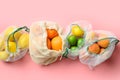 Fruits and citrics in reusable eco-friendly mesh bags on pink background. Zero waste shopping.