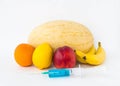 Fruits on a white background bananas, orange, melon, lemon and nectarine, next is a syringe with gmo and nitrates, genetically