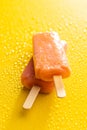 Fruity ice lolly. Sweet popsicle on yellow table with water drops