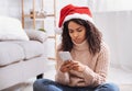 Black woman in santa hat using cellphone, looking sad Royalty Free Stock Photo