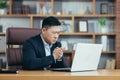 Frustrated and angry asian businessman working on laptop in office, boss shouting at laptop screen Royalty Free Stock Photo