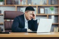 Frustrated and angry asian businessman working on laptop in office, boss shouting at laptop screen Royalty Free Stock Photo