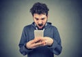 Frustrated angry man reading a text message on his smartphone feeling frustrated