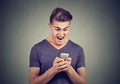 Frustrated angry man reading a text message on smartphone screaming