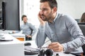 Frustrated beard man looking at computer screen and keeping his eyeglasses while sitting at his working place in office. Royalty Free Stock Photo