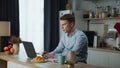 Frustrated business man feeling stressed looking at laptop screen on kitchen.