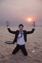 Frustrated businessman with arms outstretched kneeling in the desert at sunset