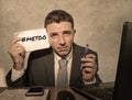 Frustrated businessman desperate at office computer desk holding notepad with the hashtag me too metoo as exploited employee Royalty Free Stock Photo