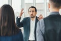 Frustrated businessman expressing despair, shouting at his employees, raising up his hands. Man and woman standing back